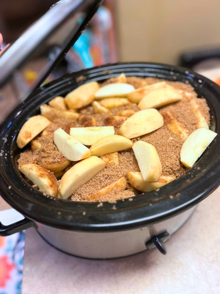 Jar of homemade slow cooker apple butter with a spoon on a rustic wooden surface