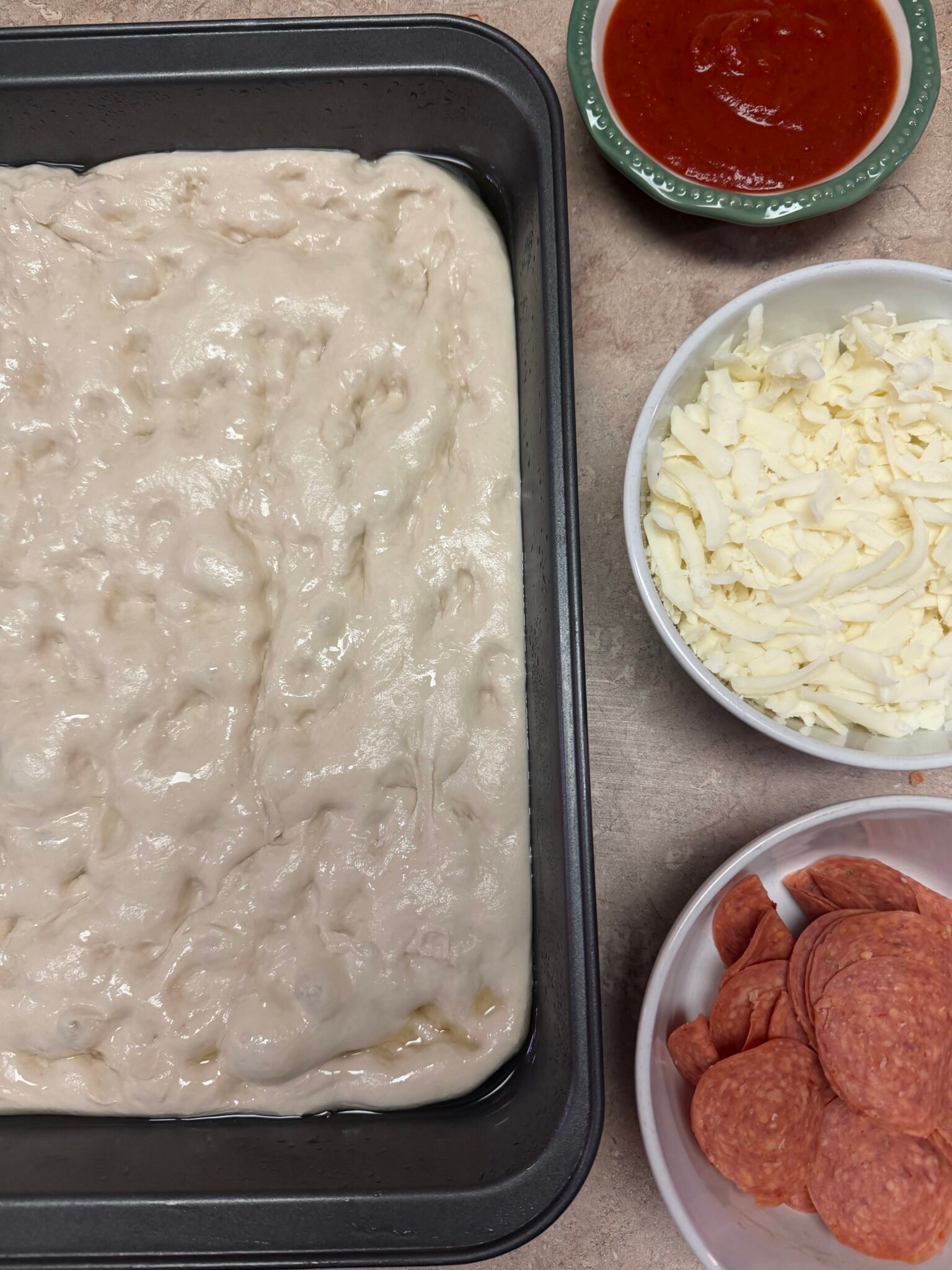 Sourdough Detroit pizza dough rising in an oiled 9x13 pan showing bubbles and airy texture